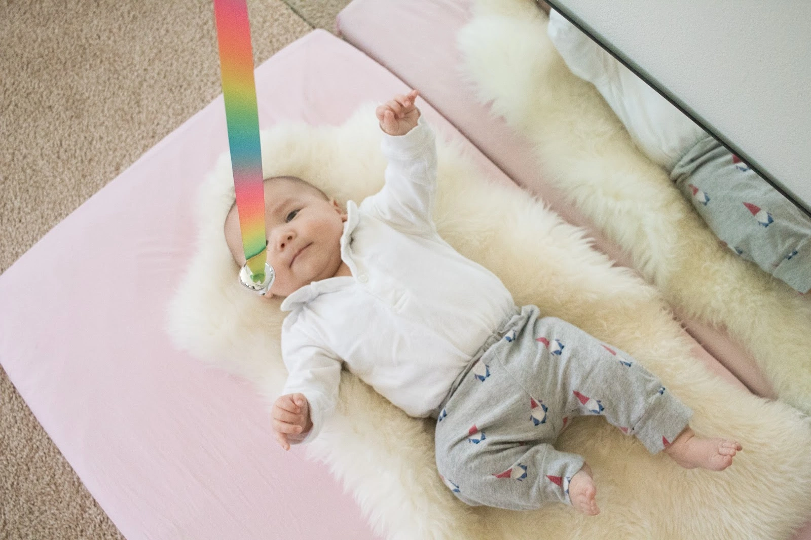 Baby lying on a floor mat reaching for a bell on a ribbon tactile Montessori mobile