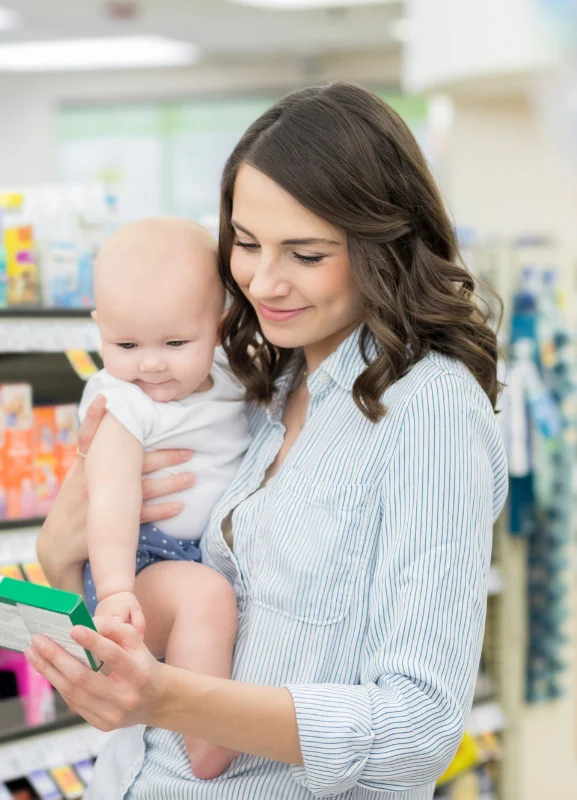 Woman holding her baby while reading the label on a product box in a store