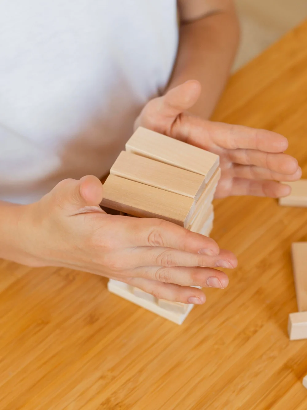 Adult's hands steadying a small stack of wooden blocks on a wooden table
