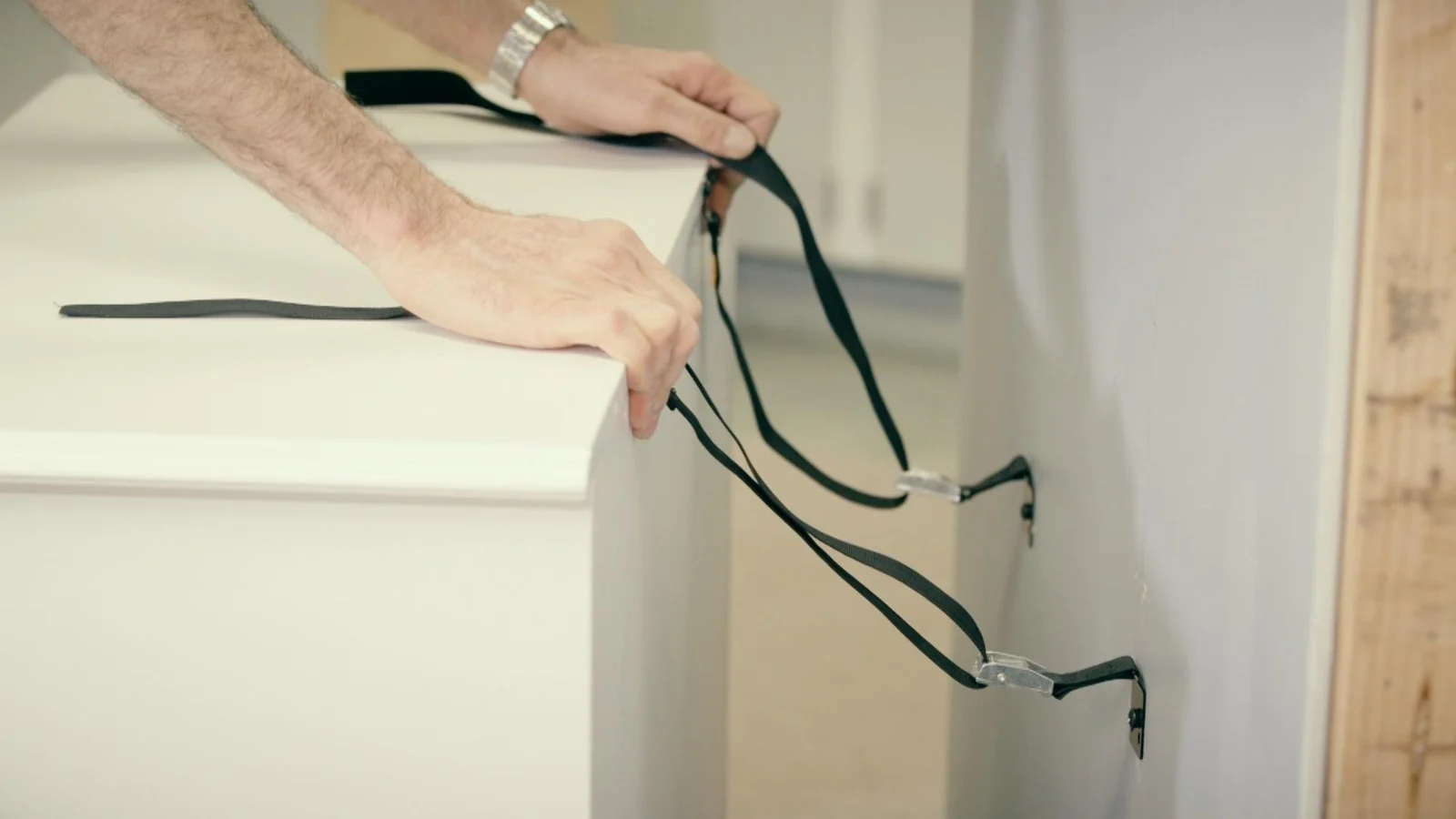 Adult attaching an anti-tip strap from the back of a dresser to the wall