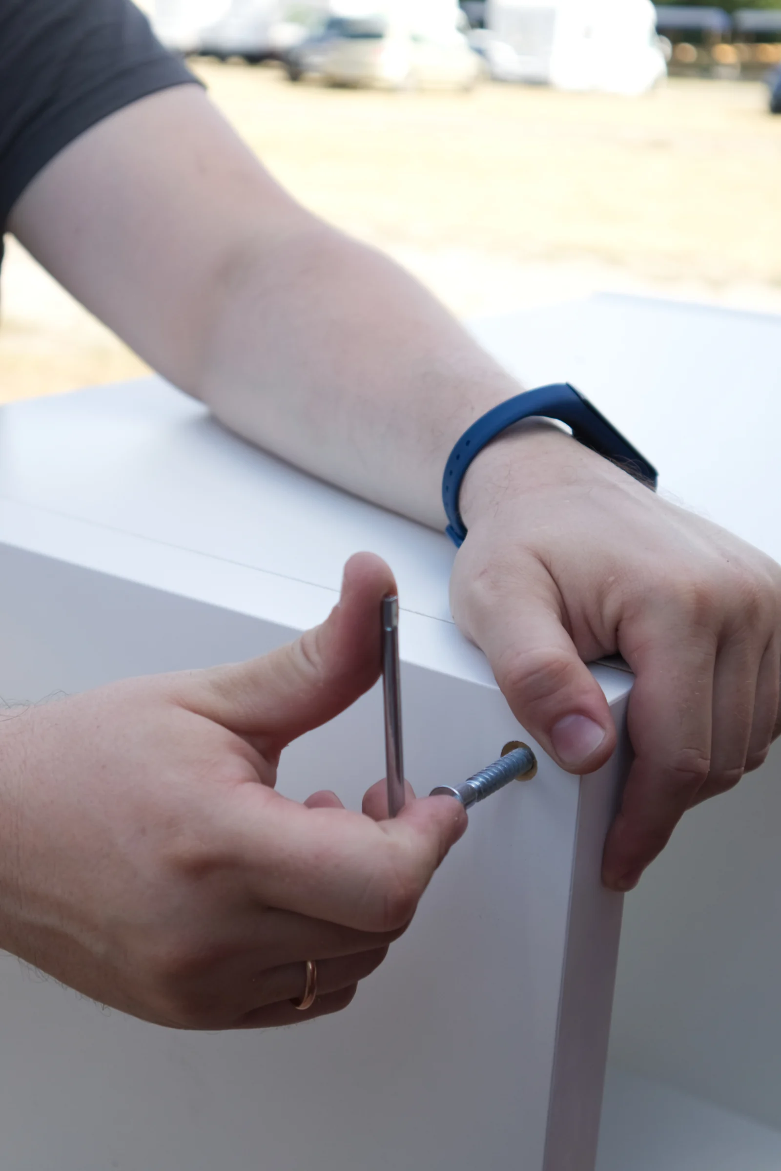 Adult hands screwing a metal L-bracket to attach a low shelf to the wall