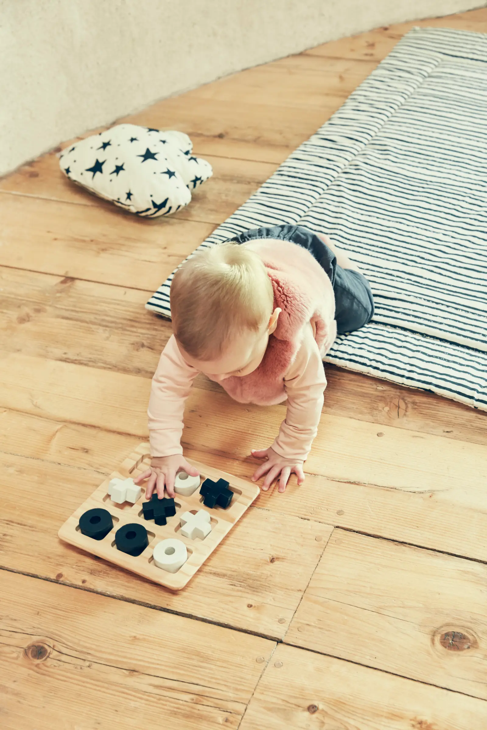 A baby on hands and knees on a wooden floor reaches for a wooden puzzle with black and white pieces