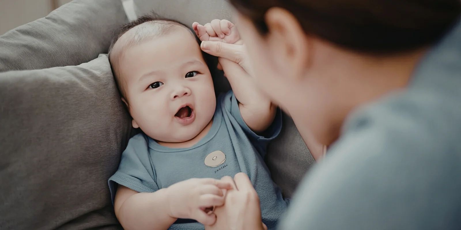 A baby lying on a blanket gazes up at a parent leaning over them