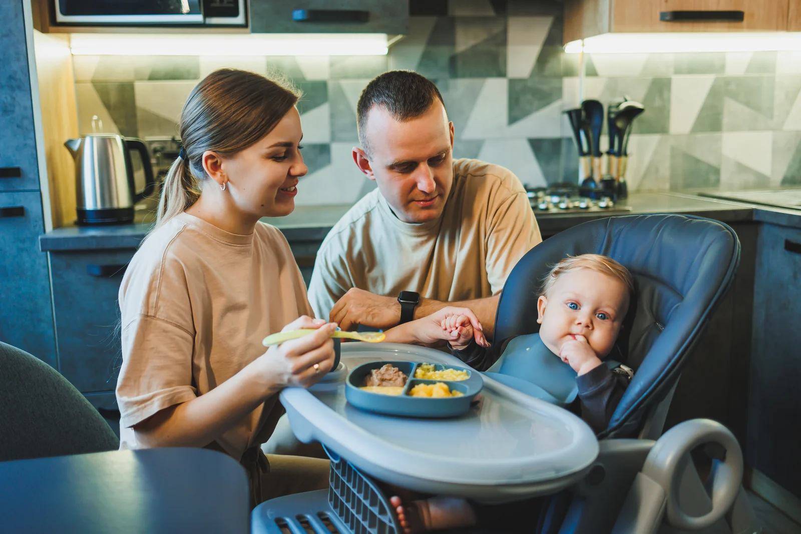 Baby sitting in a high chair pulled up to the family table, watching the adults eat