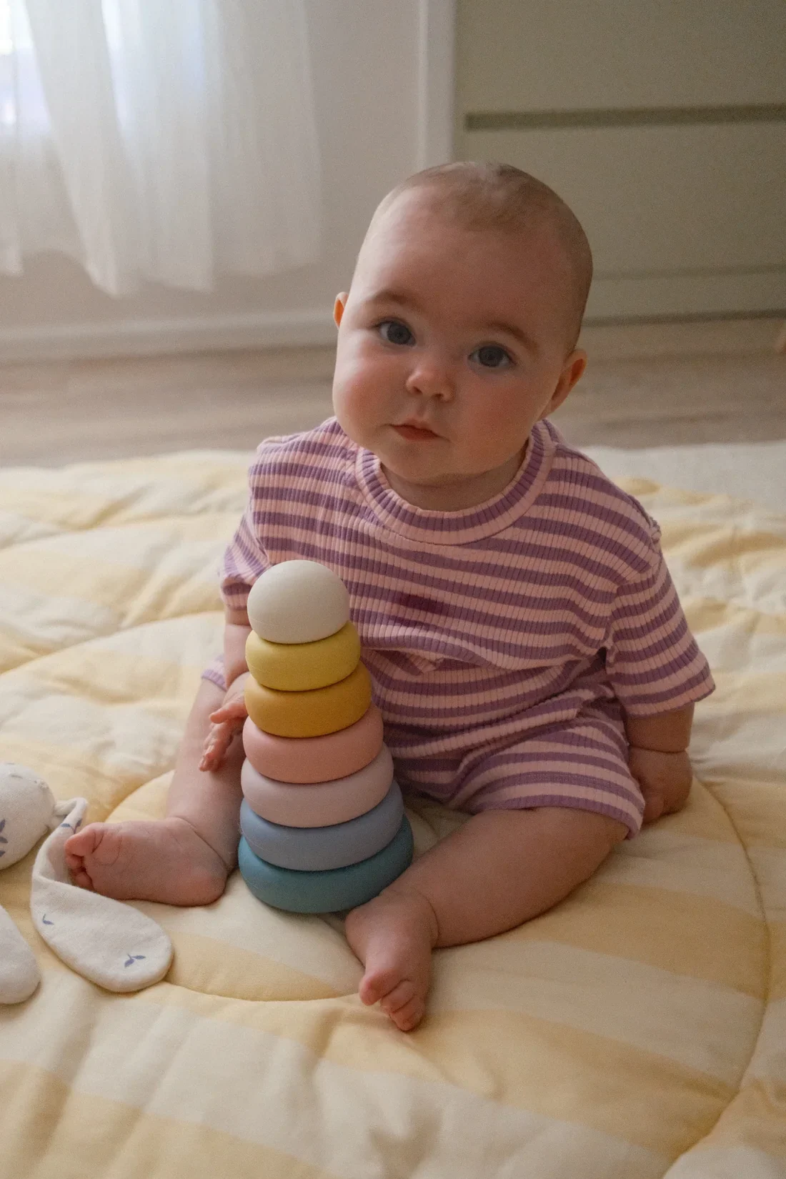 Toddler sitting on a rug, focused on sliding large wooden rings onto a ring stacker