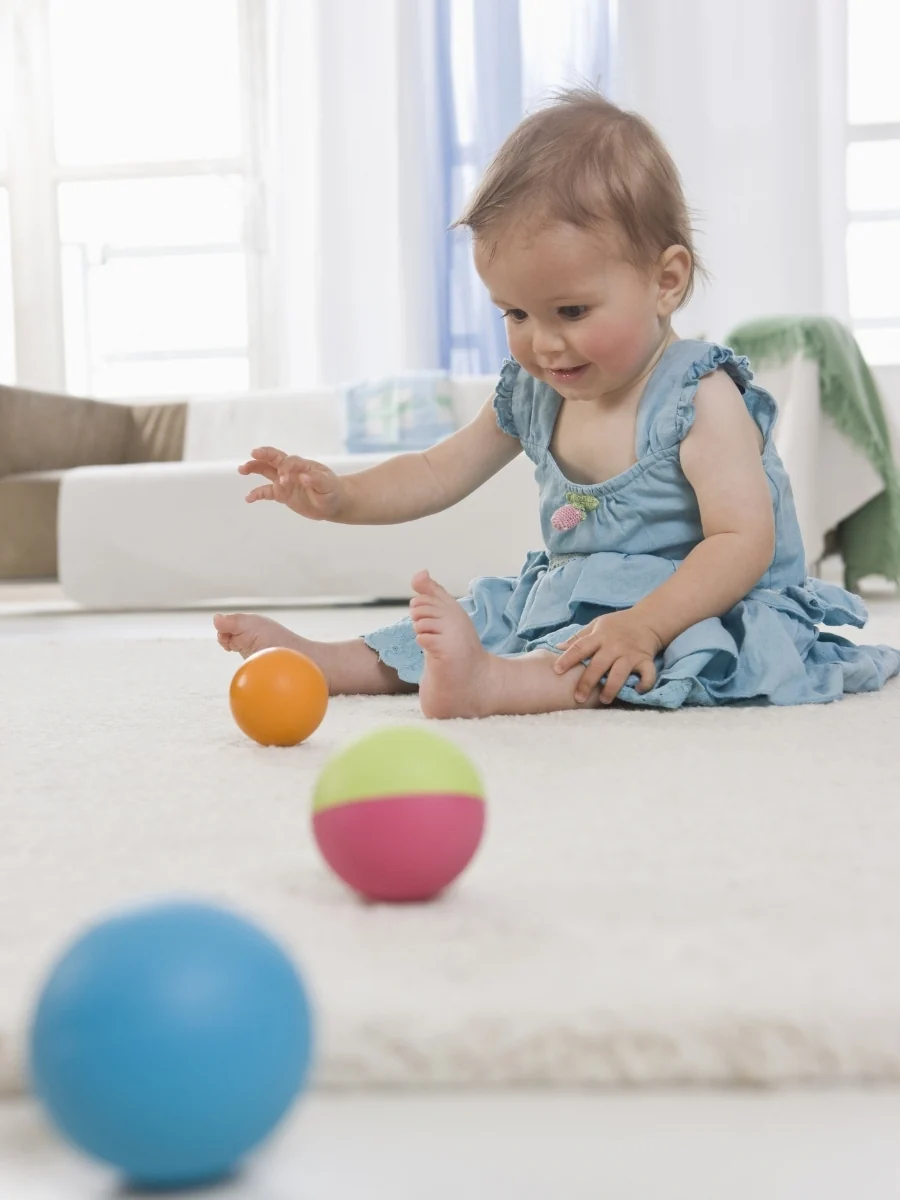 Baby sitting without support on a rug, passing a soft fabric ball from one hand to the other