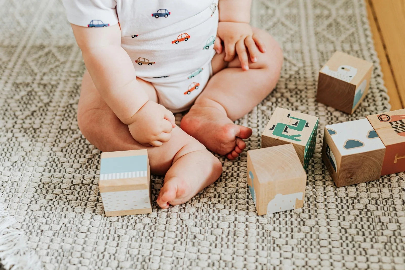 Baby sitting on a woven rug surrounded by large wooden blocks printed with animals and clouds
