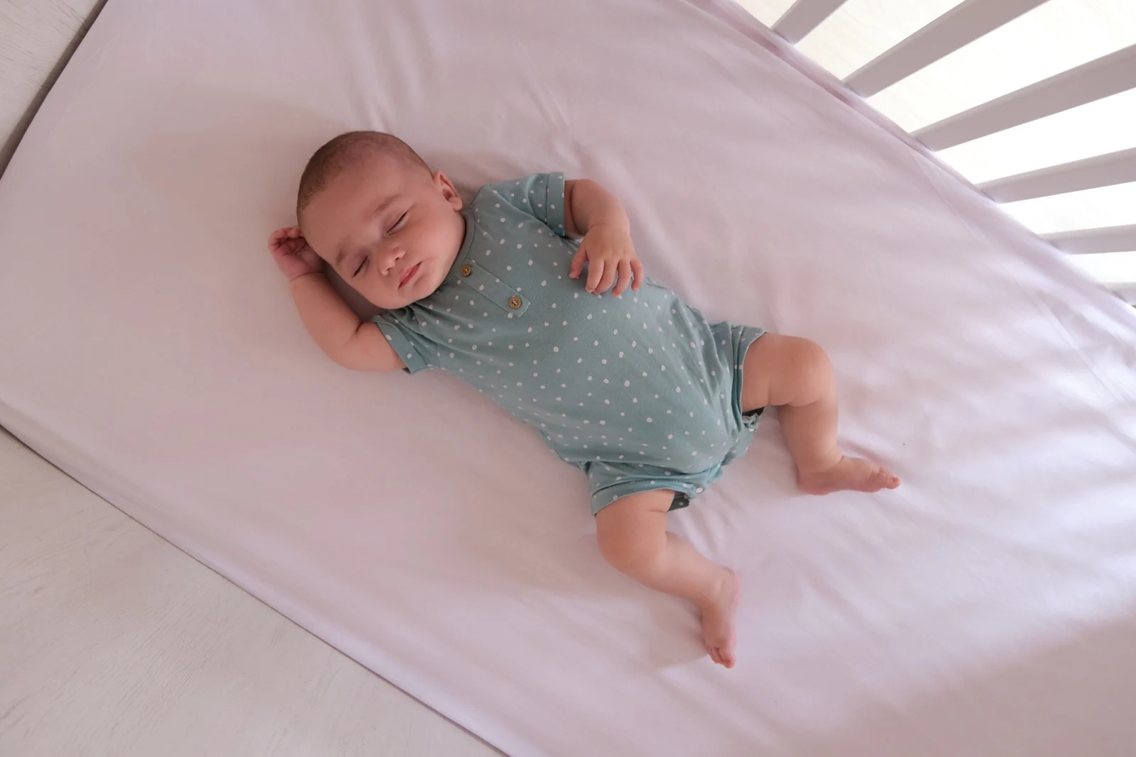 A baby asleep on their back in a crib with only a fitted sheet, no pillows or blankets