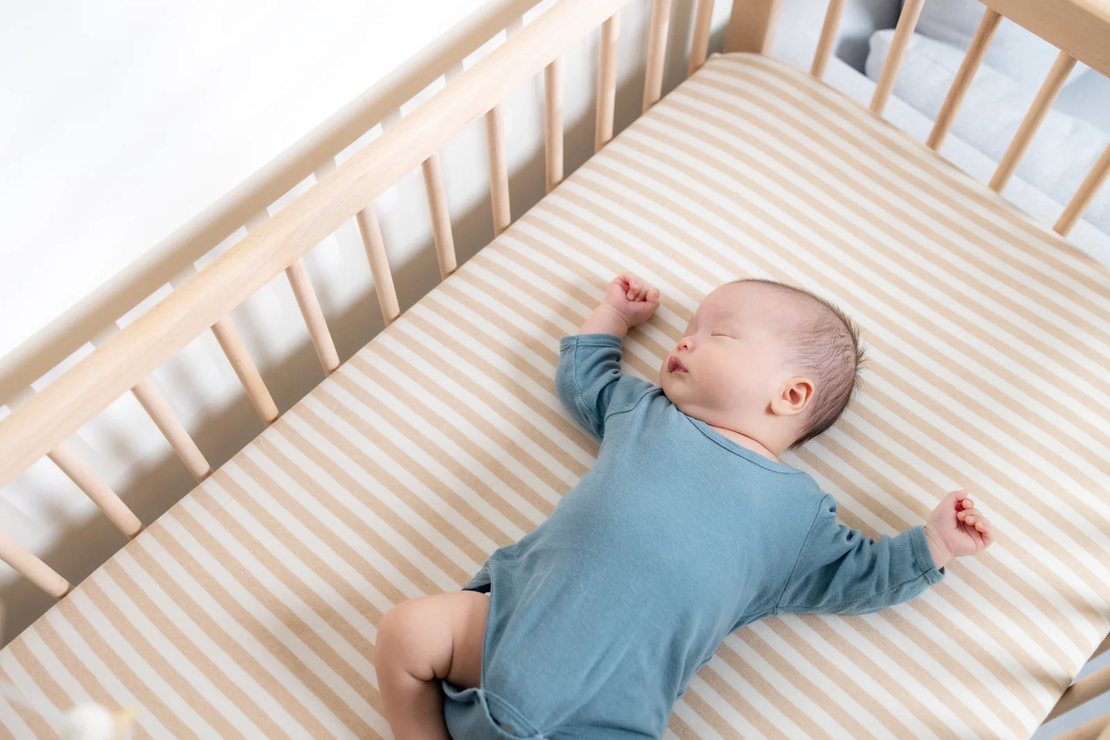 Baby asleep on their back in a crib with a fitted sheet and nothing else in it