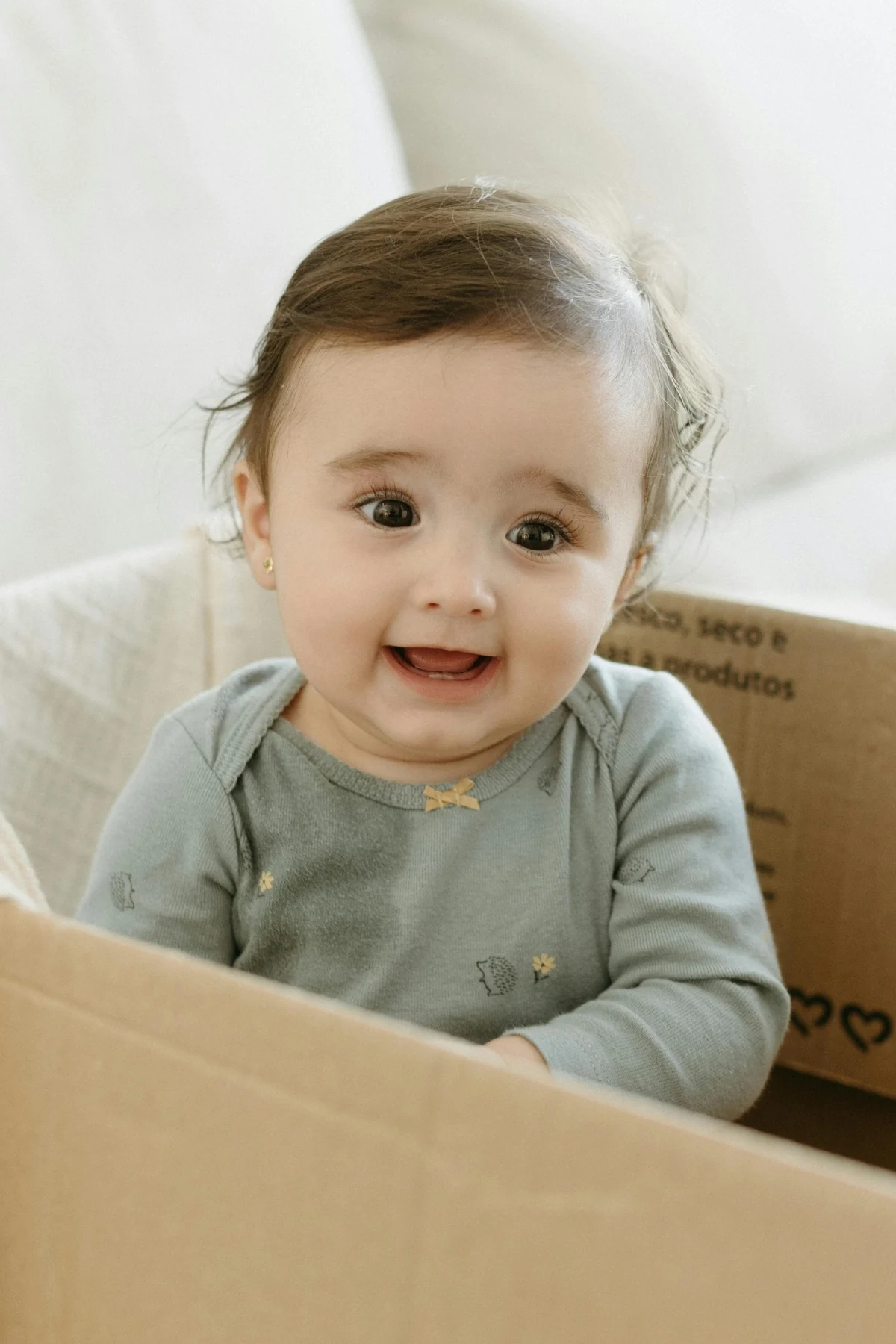 A smiling baby peeks over the edge of an empty cardboard box