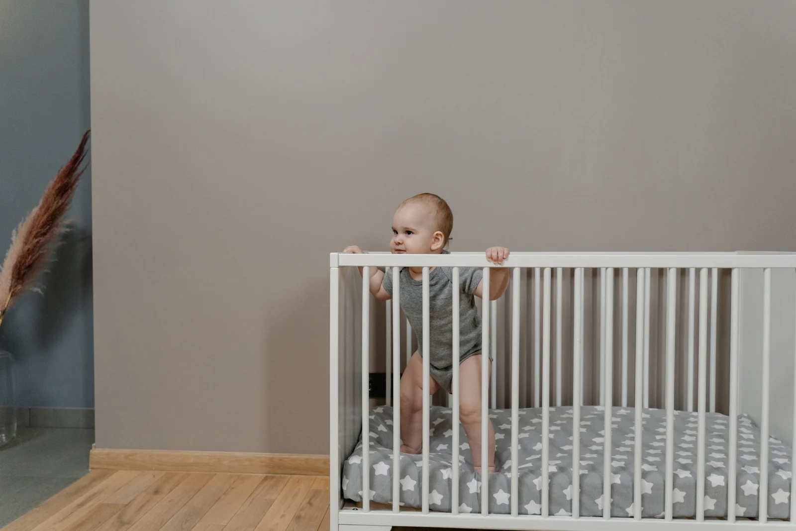 A baby standing in a crib, holding the top rail with both hands