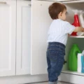 A toddler reaching for cleaning bottles in an open low kitchen cabinet: where a babyproofing checklist starts