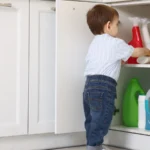 A toddler reaching for cleaning bottles in an open low kitchen cabinet: where a babyproofing checklist starts
