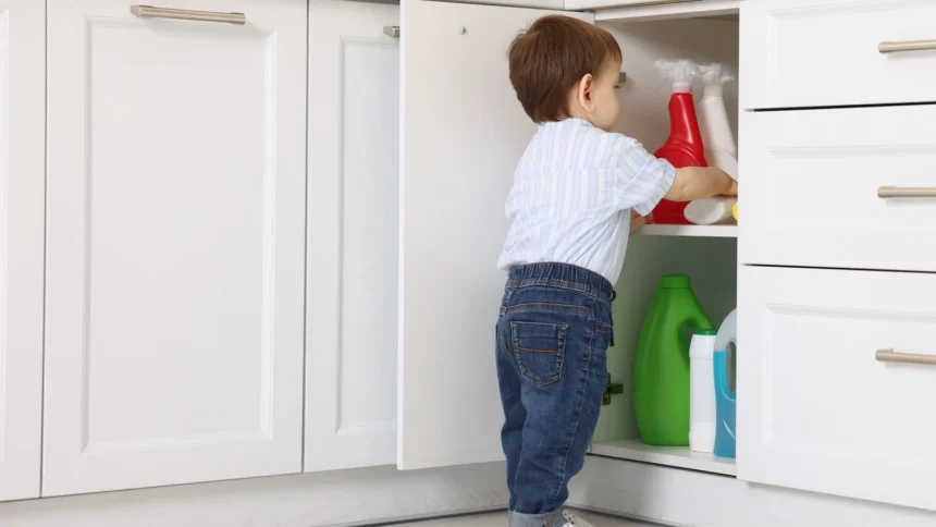 A toddler reaching for cleaning bottles in an open low kitchen cabinet: where a babyproofing checklist starts