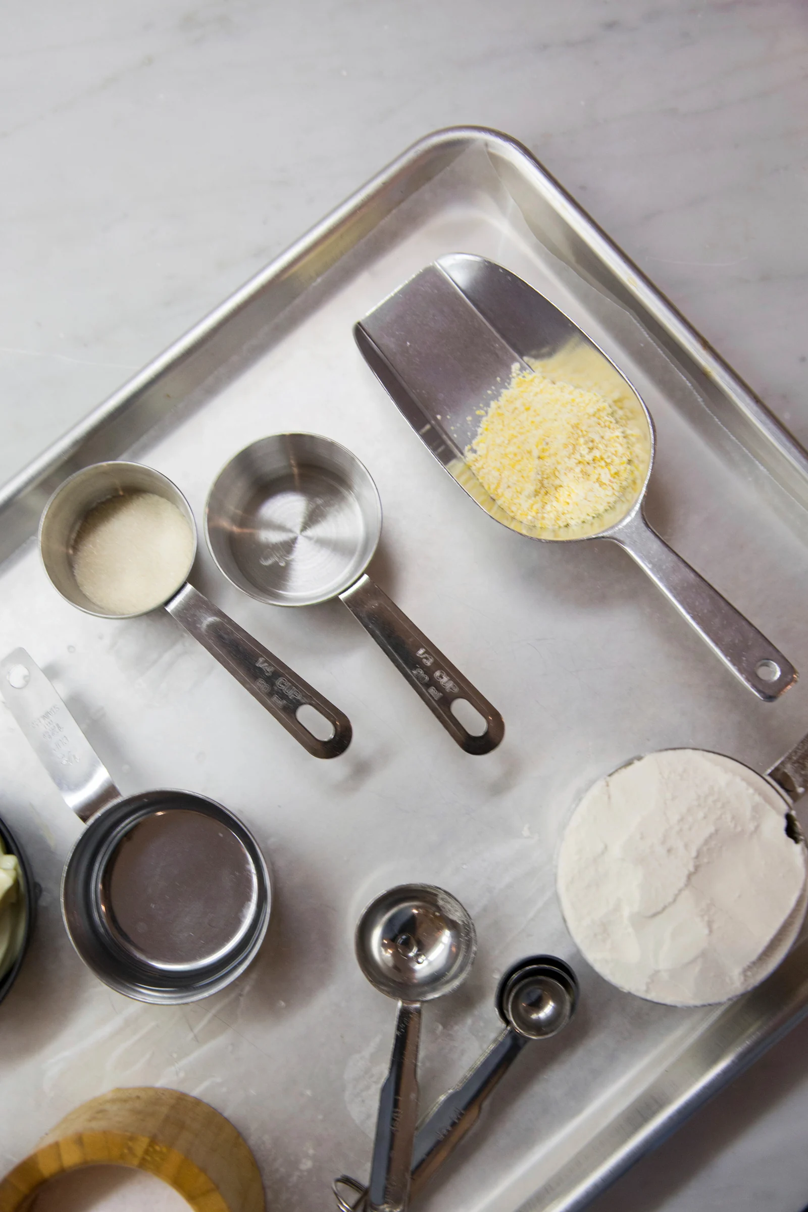 Metal baking sheet holding measuring cups, measuring spoons and a scoop on a kitchen counter