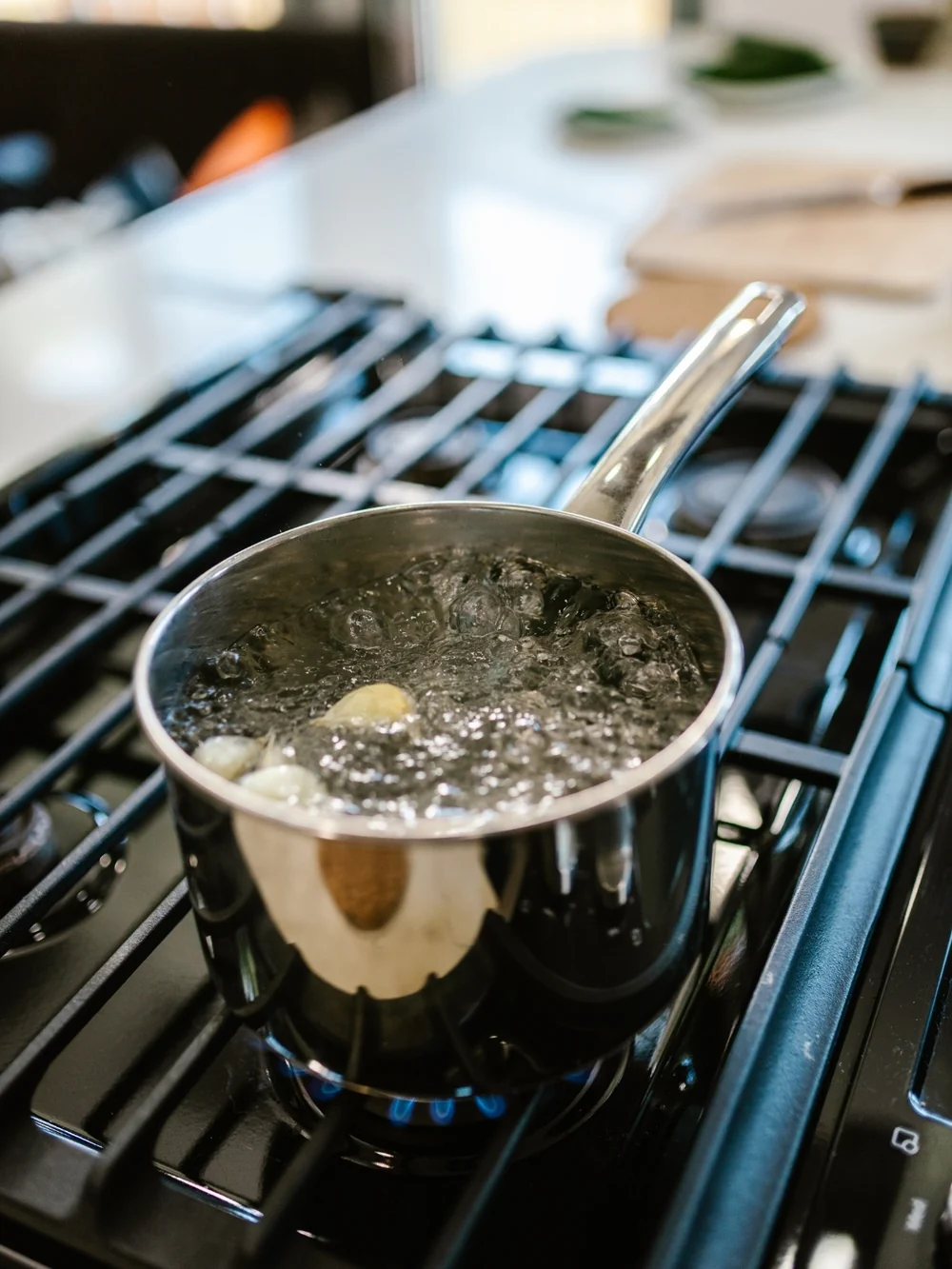 A stainless-steel saucepan of boiling water on a gas burner, its handle angled off to the side, clear of the front edge
