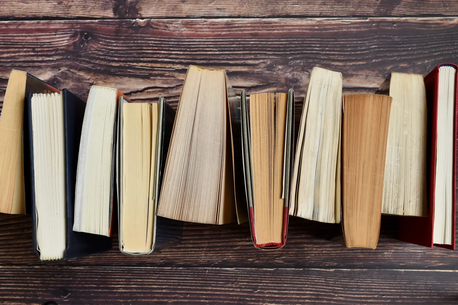 A row of old books standing side by side on a dark wooden table