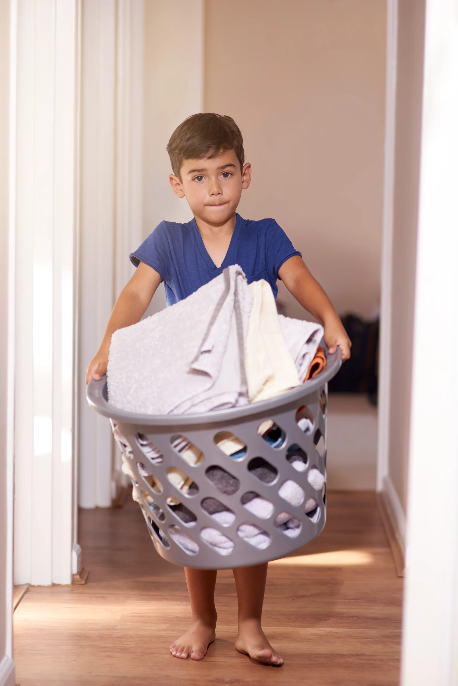 Child carrying a full laundry basket down a hallway at home