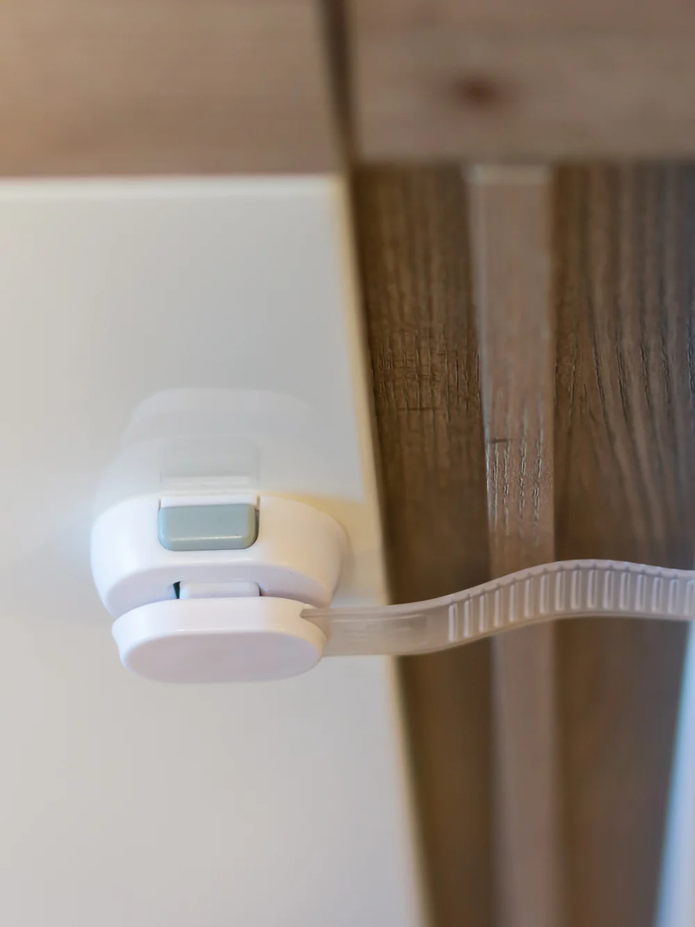 A white child safety latch strap fastened across the gap between two white cabinet doors