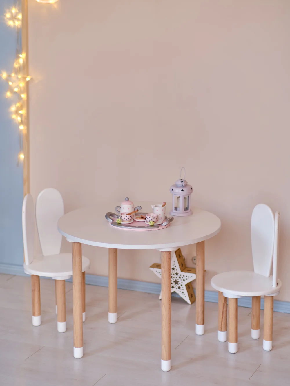 Child-size wooden table and chairs in a sunny room with a low shelf behind them