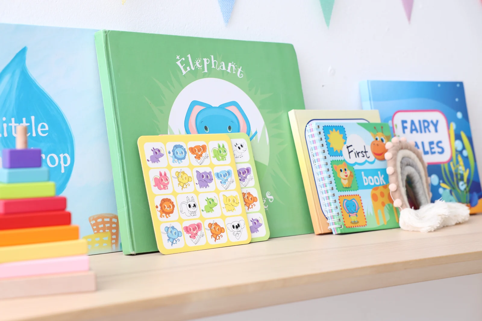 Colorful children's books standing cover-out on a light wooden shelf beside a wooden stacking toy