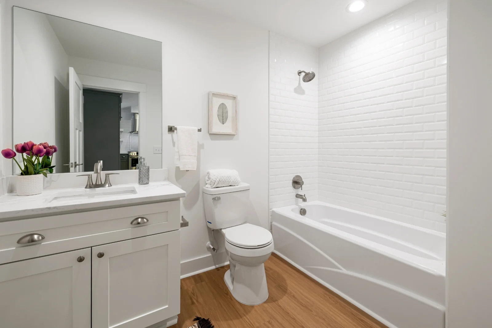 A bright family bathroom with a closed toilet lid, a white vanity and a bathtub with a tiled wall
