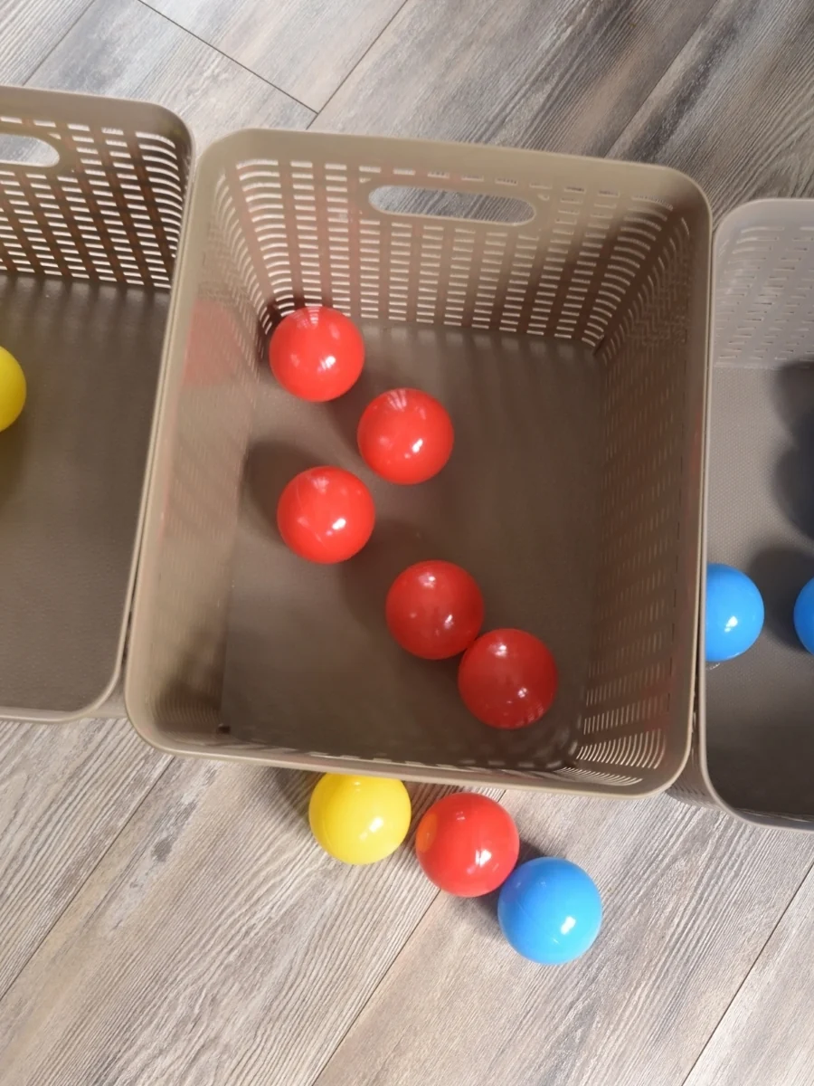 Red, yellow and blue plastic balls sorted by color into beige baskets on a wood floor