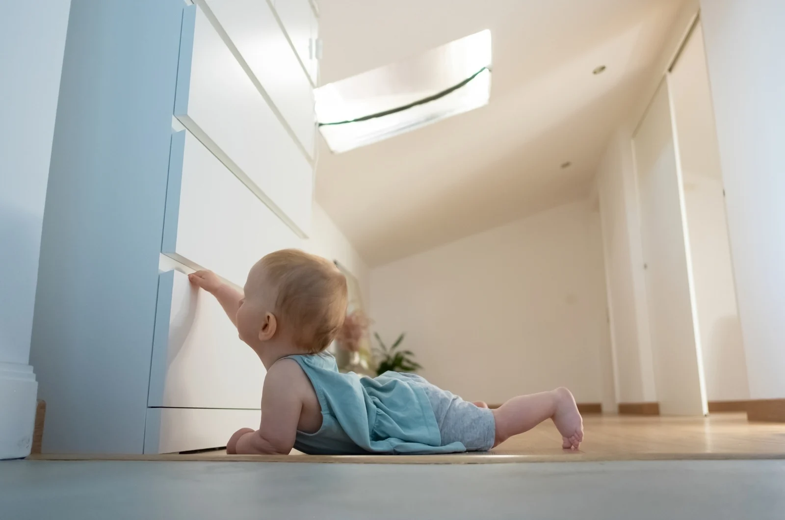Low view from floor level of a baby on their tummy, reaching up to pull a dresser drawer