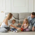 A family of four plays together on a rug in a bright living room: a Montessori playroom corner