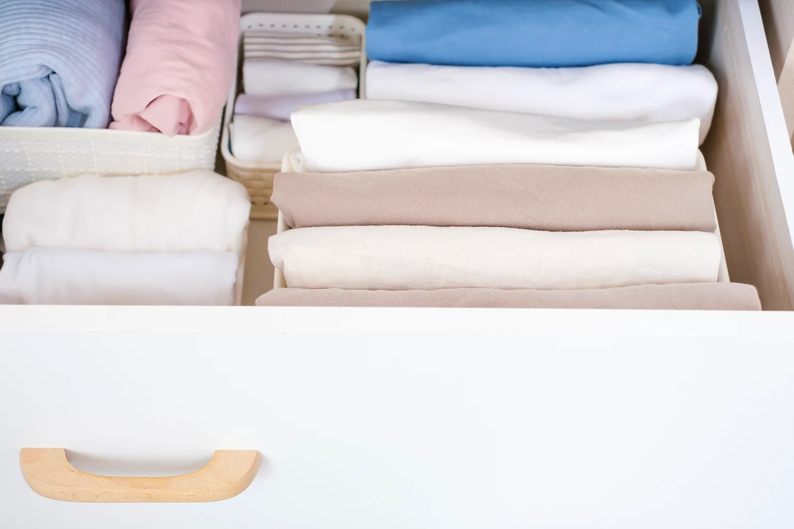 Folded clothes and linens in whites, beige and soft blue stacked upright in an open white dresser drawer