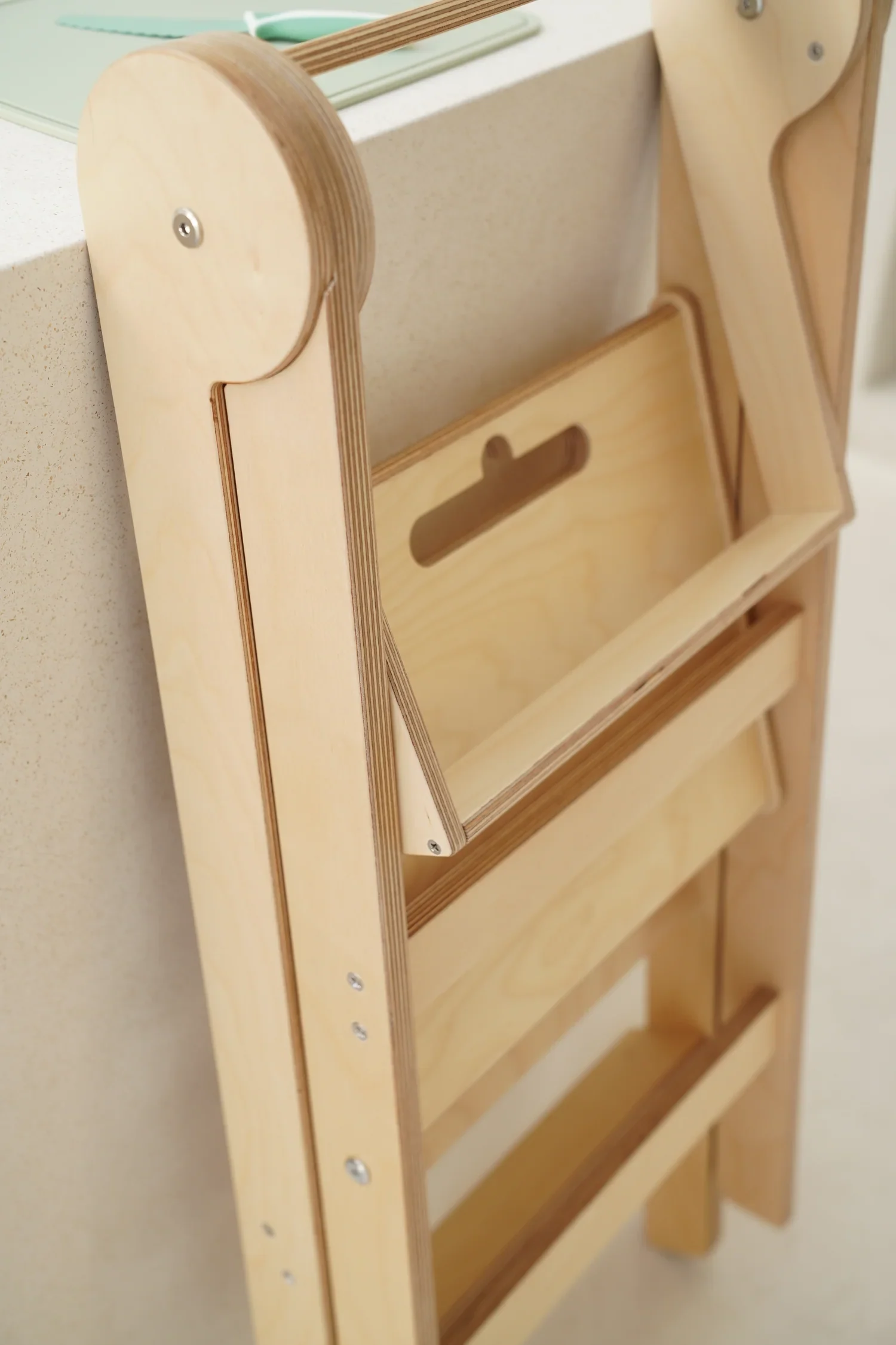 A wooden folding kitchen tower, folded flat and leaning against the side of a counter