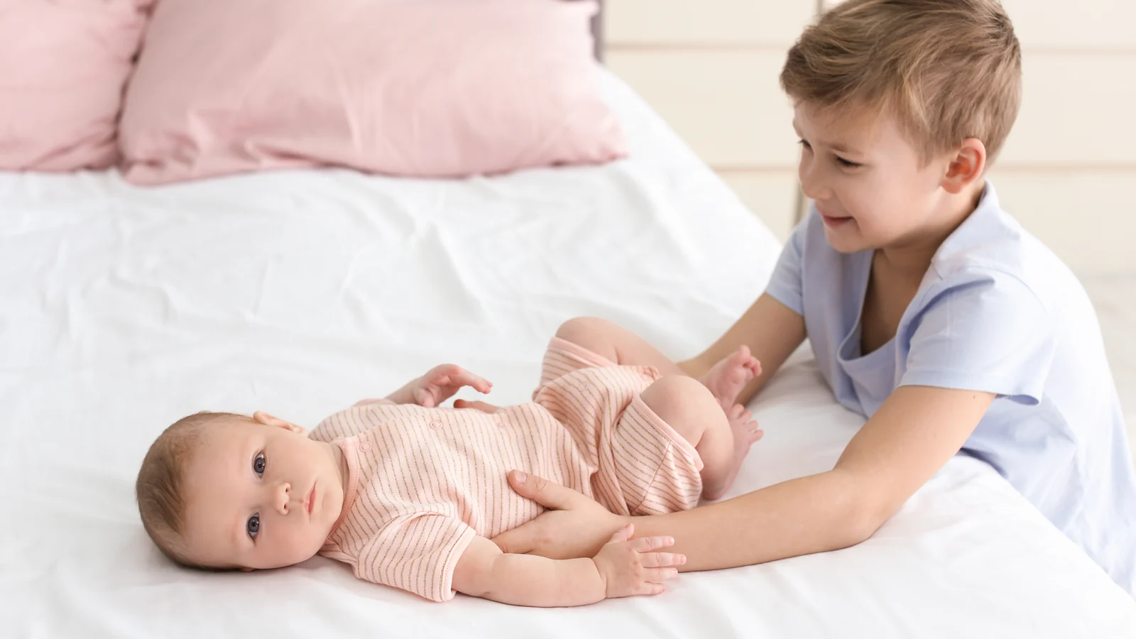 Big brother resting a hand on a newborn lying on a bed: fun activities for siblings to do together
