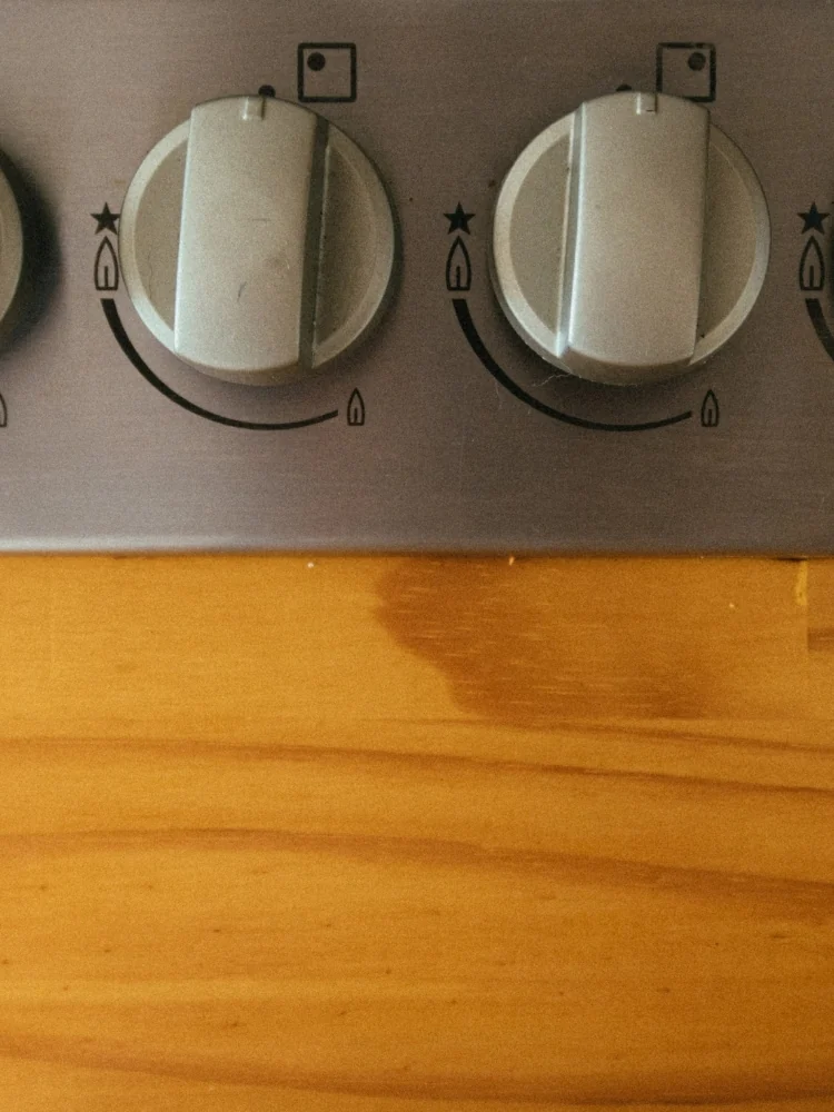 Close-up of two round control knobs on the front panel of a gas stove, above a wooden countertop