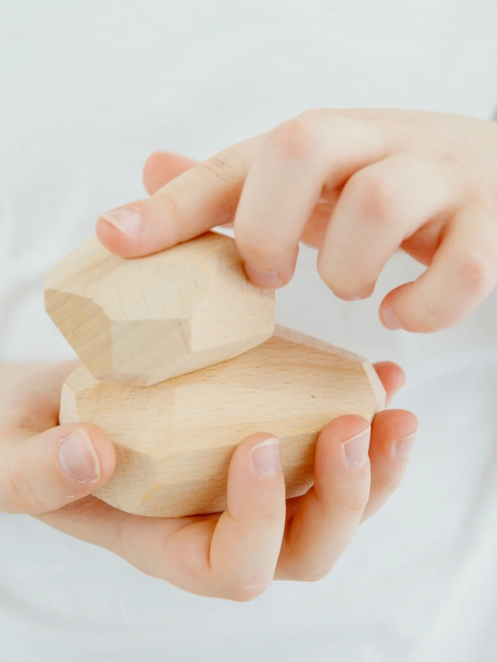 Two hands hold smooth wooden stacking stones, one resting on top of the other