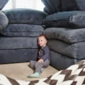 Toddler sitting beside a fort built from stacked sofa cushions in a living room: indoor activities for toddlers