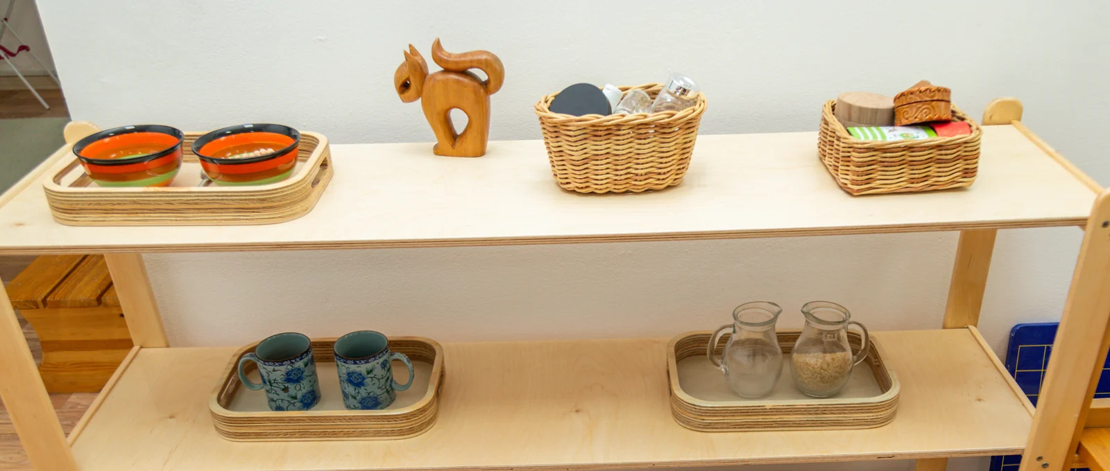 Low open wooden shelf holding a few things: two bowls on a tray, a wooden squirrel, two baskets, two cups and two small pitchers