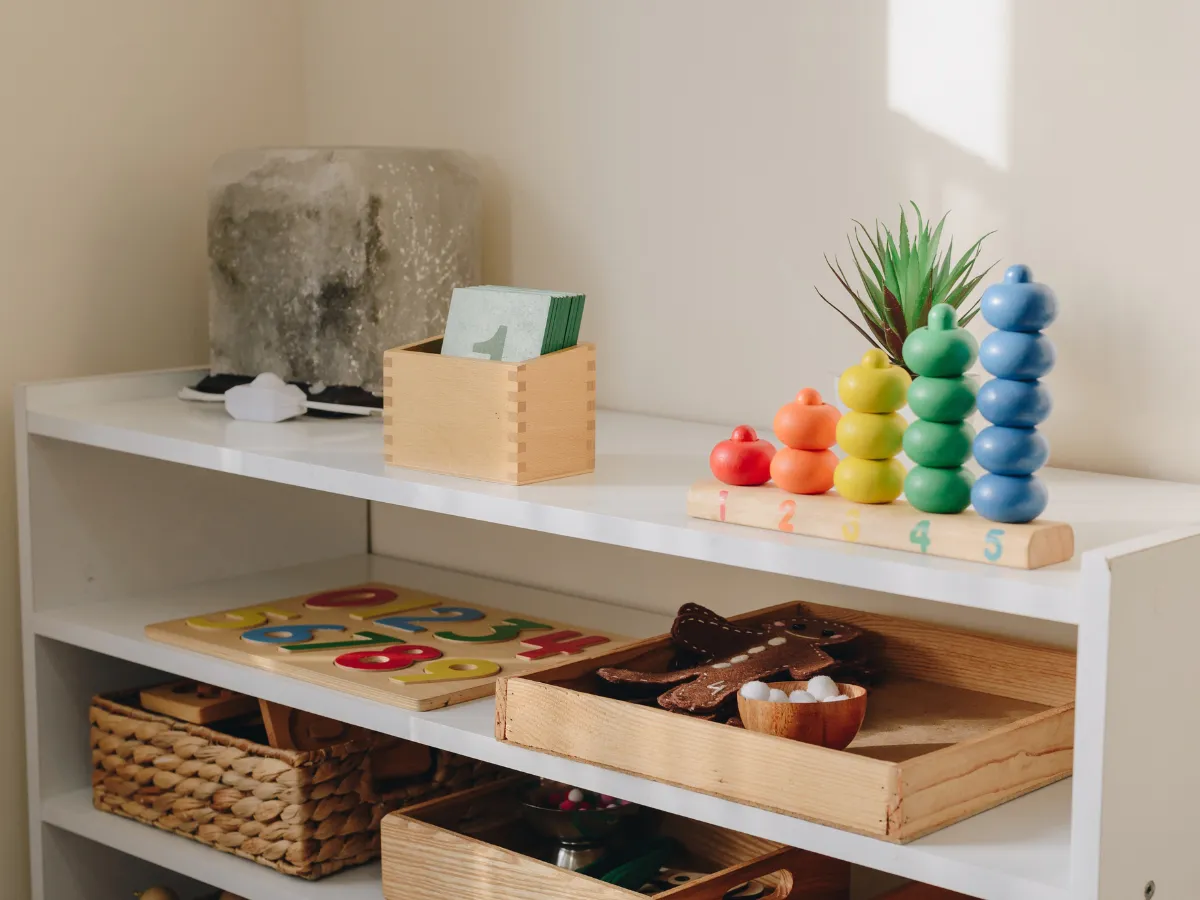 A low white shelf with a few wooden toys, trays and a basket set out at a child's height