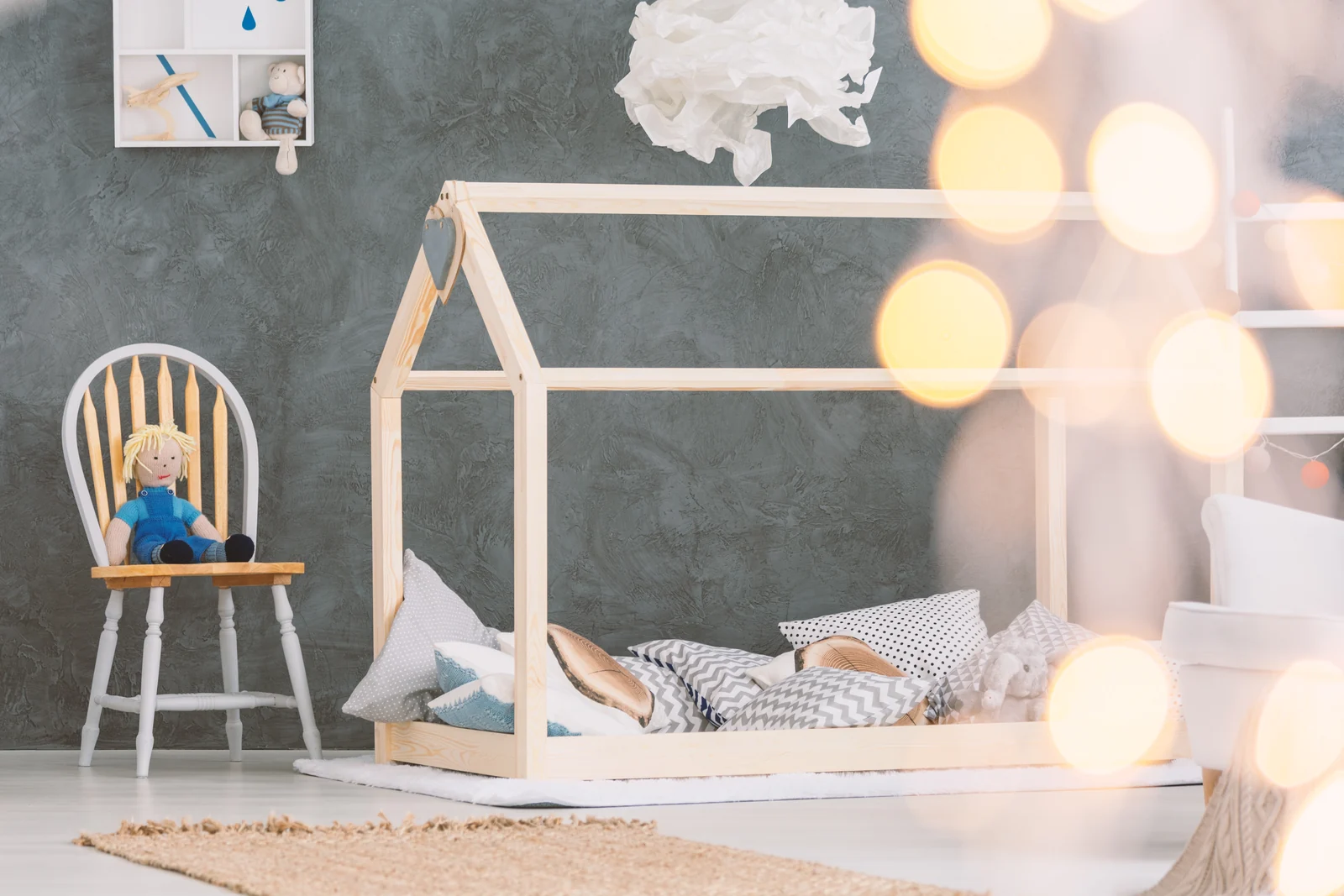 A low wooden house-shaped bed frame in a child's room, with pillows and a soft toy on the mattress
