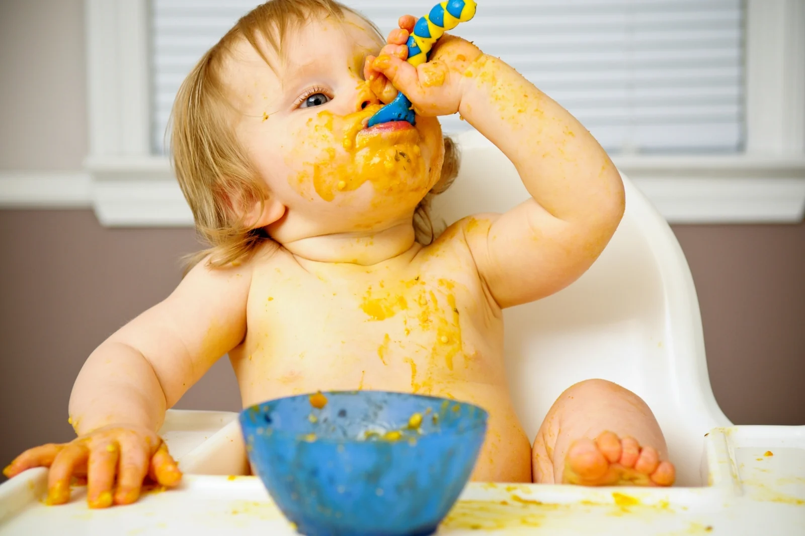 Toddler with food on hands and face sitting in a high chair