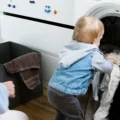 Toddler pulling clothes out of a laundry machine as a parent kneels nearby: Montessori activities at home