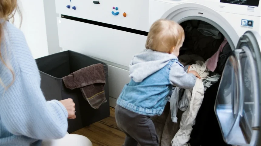 Toddler pulling clothes out of a laundry machine as a parent kneels nearby: Montessori activities at home