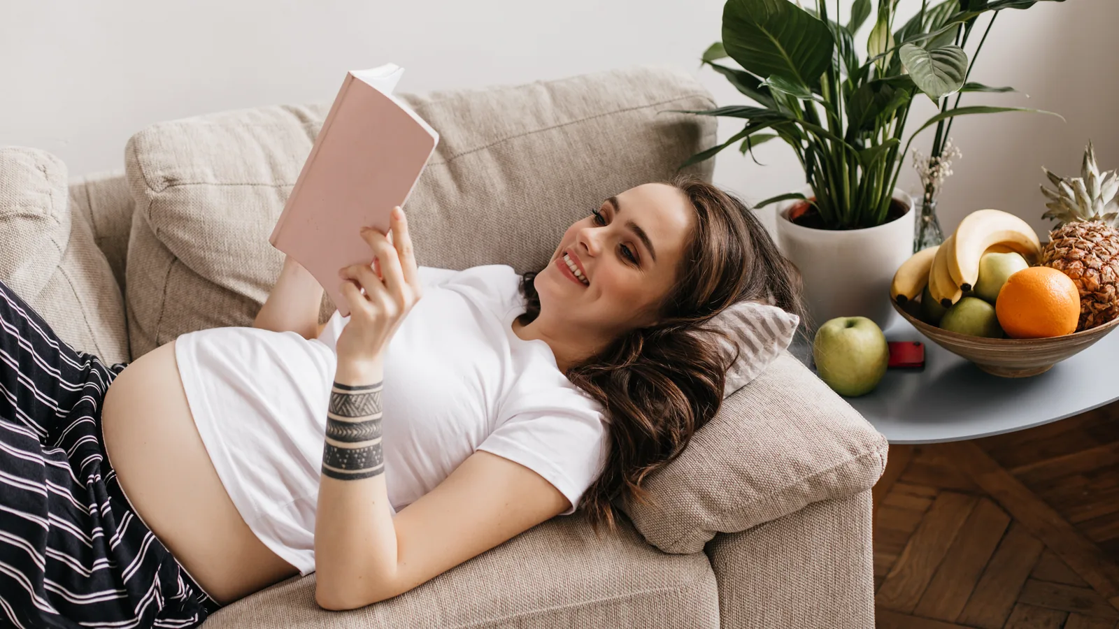 A pregnant woman lies on a sofa reading a book in daylight: Montessori books for parents
