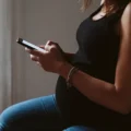 Pregnant parent sitting by a window, reading about Montessori criticism on a phone