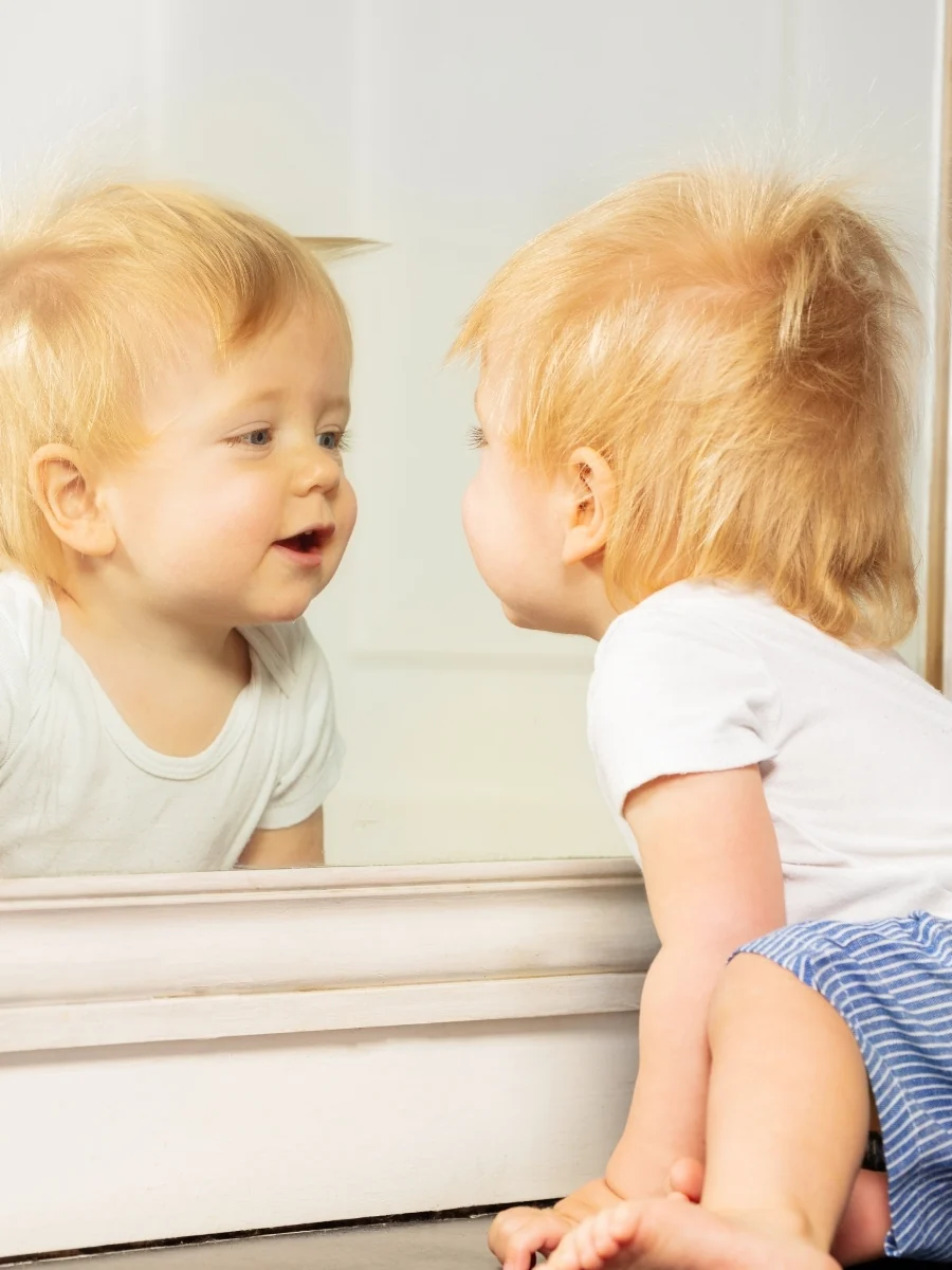 Baby kneeling at a floor-length mirror and looking at their reflection