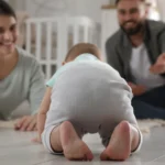 Two smiling parents on a bright wood floor watch a baby crawl toward them: a Montessori observation journal starts with watching