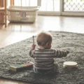 A baby in a striped top plays with a toy xylophone and a tambourine on a living room rug: Montessori on a budget