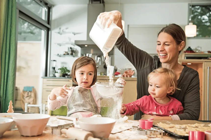Montessori parenting style in real life: a parent pours flour as a preschooler sifts it and a toddler reaches in to help