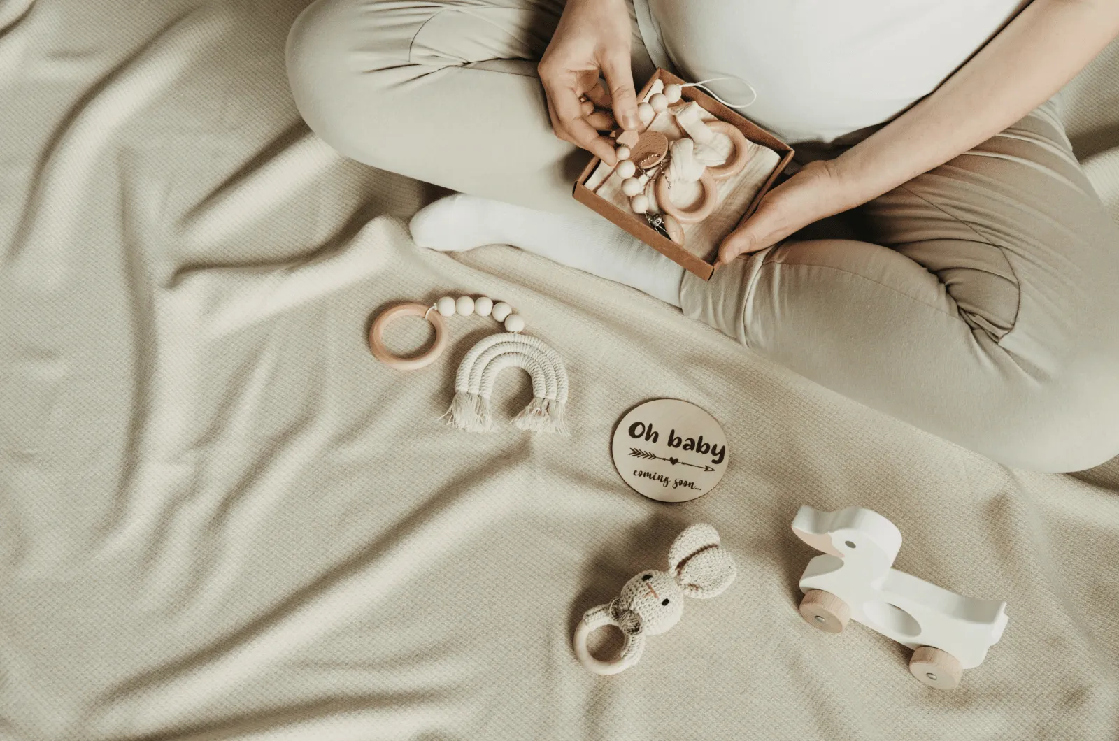 Pregnant person resting a hand on their bump beside a small basket of simple wooden baby toys