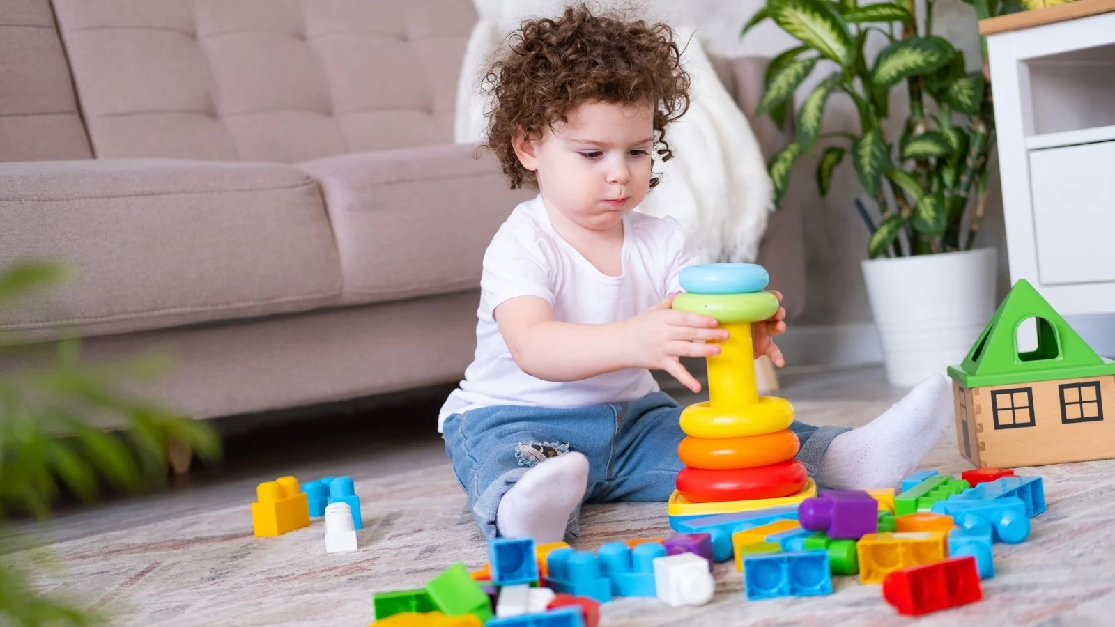Toddler on a rug, focused on stacking rings onto a stacker, the kind of focus Montessori sensitive periods describe