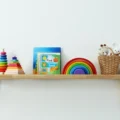 Montessori vs Waldorf toys on one simple shelf: ring stackers, a wooden rainbow, a board book and a basket of soft toys
